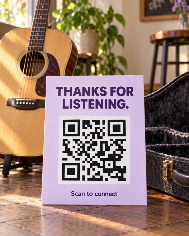 A lavender Thanks for listening sign with a QRown demo QR beside an acoustic guitar and its case.